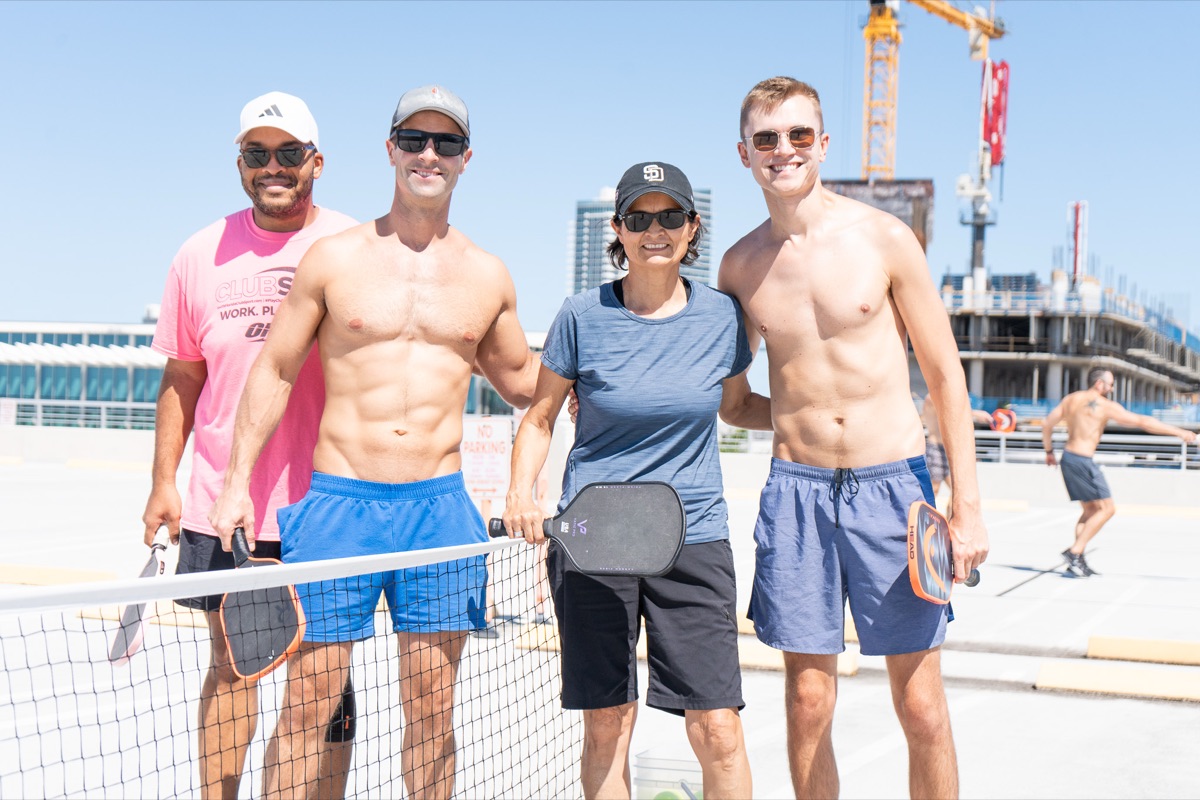 A group of gay and queer pickleball players posing with paddles at the net in Miami Beach