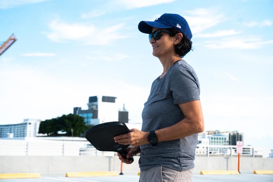 A woman pickleball player ready at the line with her paddle and the Miami skyline behind her