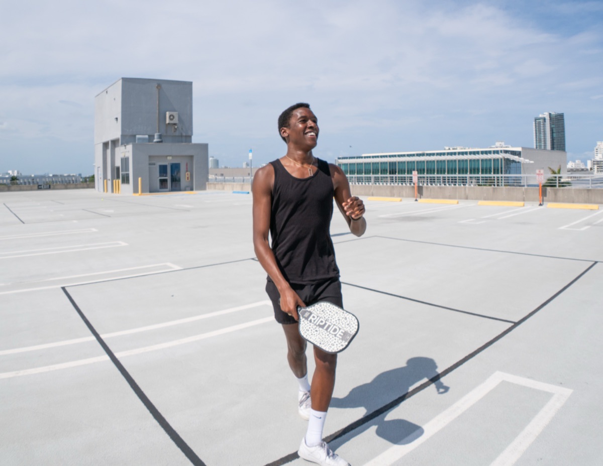 A smiling pickleball player walking the court with his paddle on a sunny Miami Beach rooftop