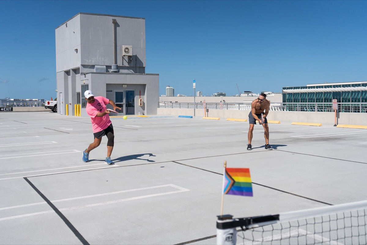 Two players rally across the net with a Progress Pride flag flying on the net post in Miami Beach
