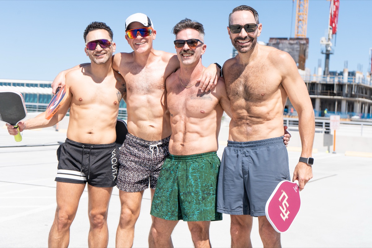 Four friends from our queer pickleball community with paddles, arms around each other in the sun